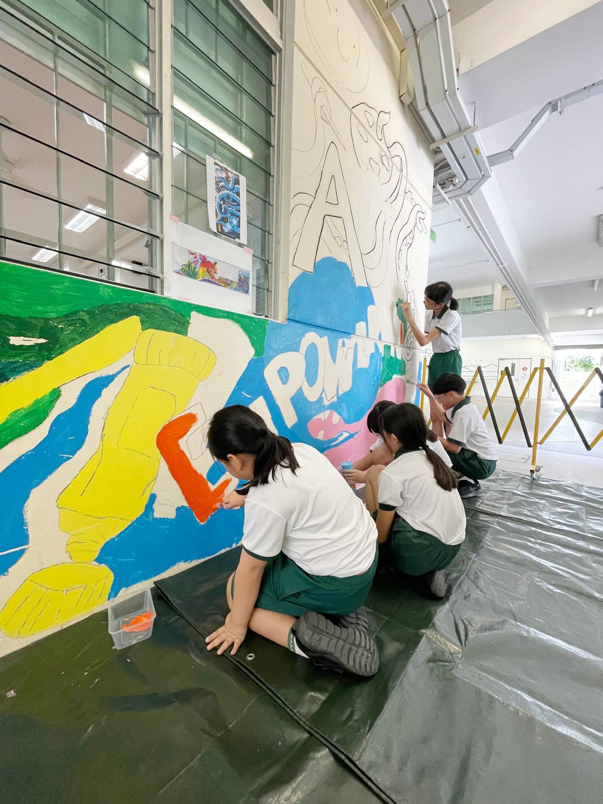 Students work together to paint a large colourful mural on a school wall, expressing creativity through collaborative art.